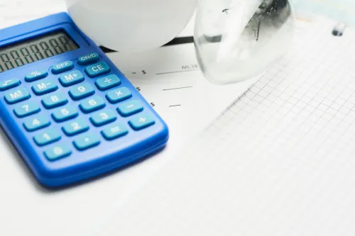 Calculadora, lâmpada e caderno sobre uma fatura de eletricidade